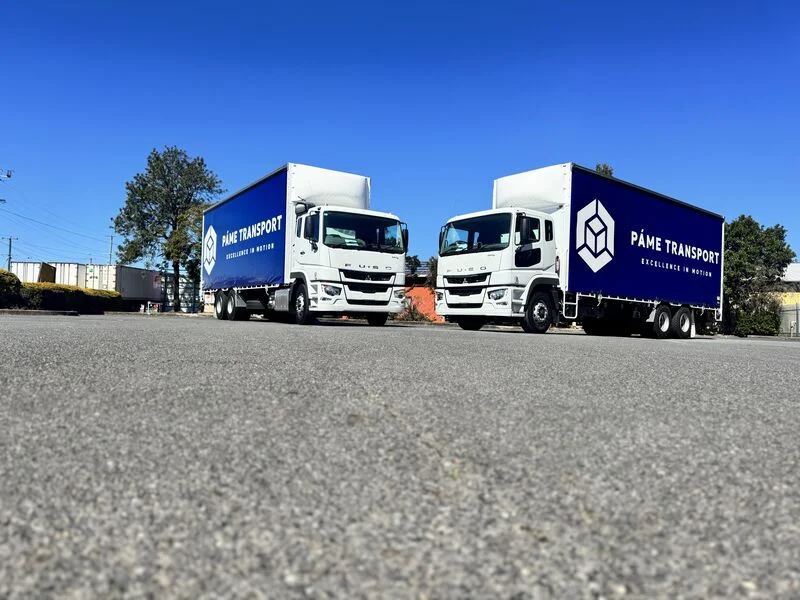 Two Páme Transport branded curtain-sider trucks parked side by side
